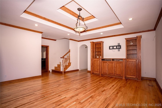 interior space featuring baseboards, stairs, a tray ceiling, light wood-style floors, and arched walkways