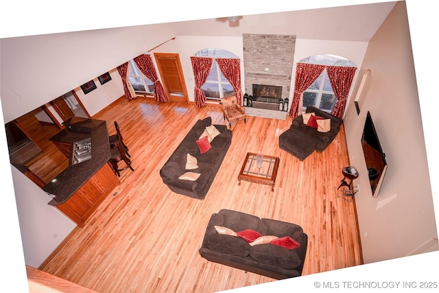 living room featuring a stone fireplace, lofted ceiling, and wood finished floors