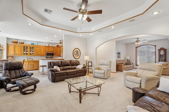 living room with visible vents, arched walkways, a raised ceiling, and a ceiling fan