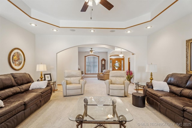 living area featuring a raised ceiling, arched walkways, and ceiling fan