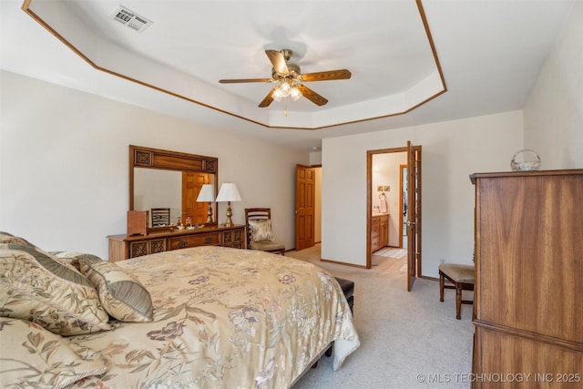 bedroom with visible vents, a tray ceiling, ensuite bath, baseboards, and light colored carpet