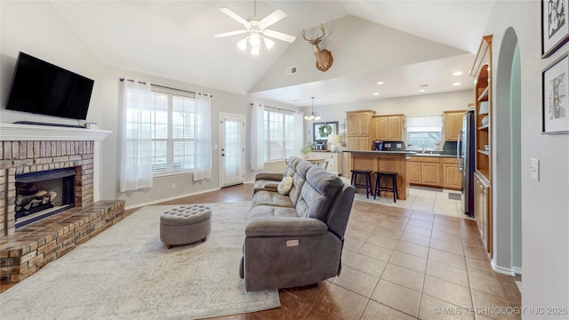 living room with visible vents, high vaulted ceiling, ceiling fan with notable chandelier, a fireplace, and light tile patterned floors