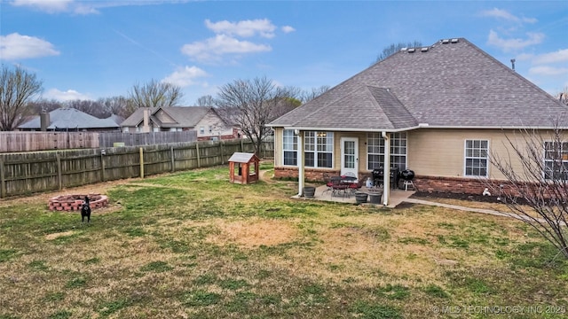 rear view of property with a lawn, a fenced backyard, an outdoor fire pit, roof with shingles, and a patio area