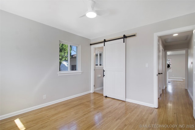 unfurnished bedroom featuring light wood finished floors, ceiling fan, baseboards, and a barn door