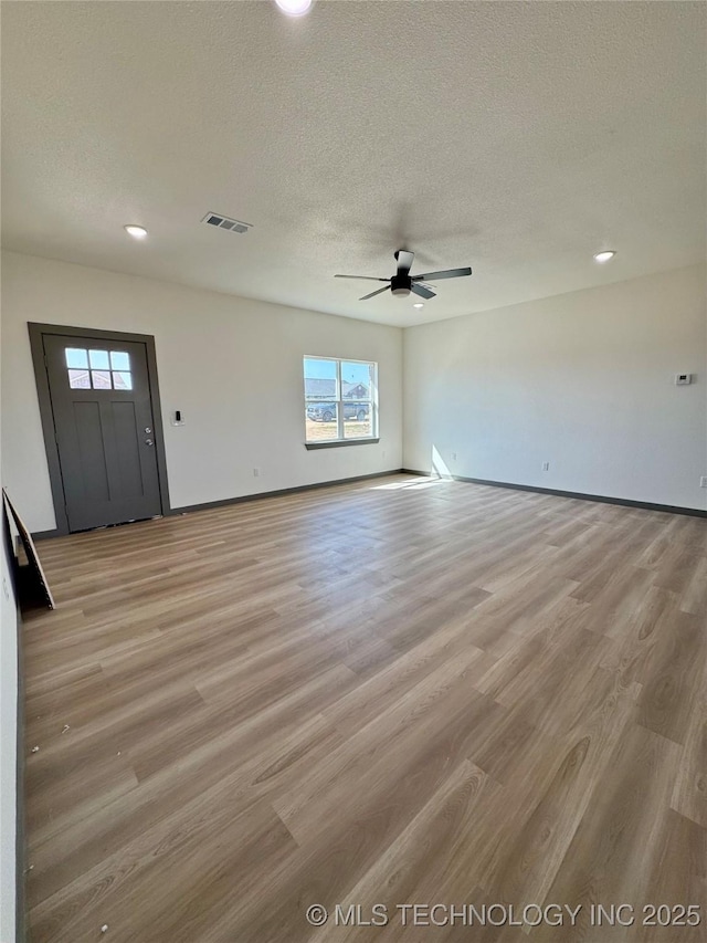 interior space featuring visible vents, a ceiling fan, light wood-type flooring, and a textured ceiling