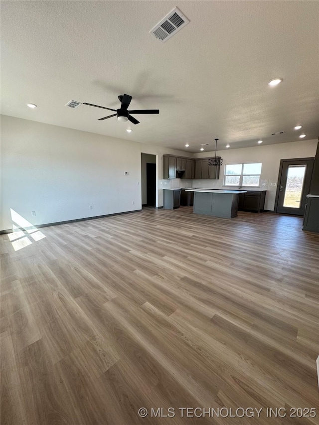 unfurnished living room featuring visible vents, a textured ceiling, light wood-style flooring, and a ceiling fan