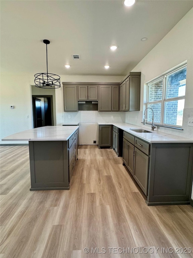 kitchen featuring under cabinet range hood, gray cabinetry, light wood-style floors, and a sink