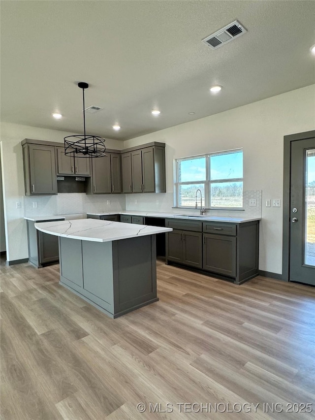 kitchen featuring visible vents, gray cabinets, a sink, a center island, and light wood-style floors