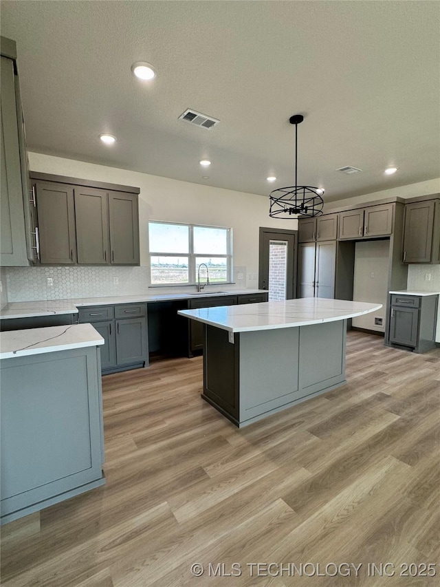 kitchen featuring visible vents, gray cabinets, a kitchen island, and light wood-style floors