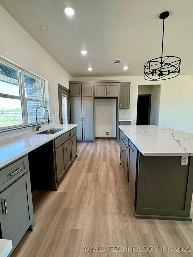 kitchen with light wood finished floors, gray cabinetry, a center island, recessed lighting, and a sink