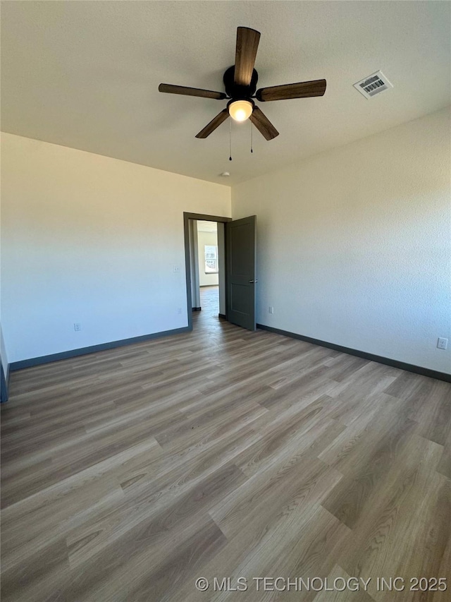 unfurnished room featuring wood finished floors, a ceiling fan, visible vents, and baseboards