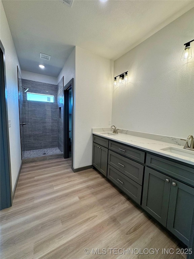 bathroom featuring tiled shower, wood finished floors, baseboards, and a sink