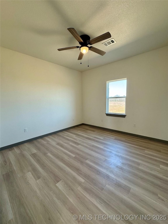 spare room with visible vents, a ceiling fan, a textured ceiling, wood finished floors, and baseboards