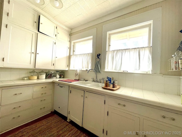 kitchen with a sink, backsplash, white cabinetry, dishwasher, and tile counters