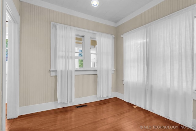unfurnished room with baseboards, wallpapered walls, wood finished floors, and visible vents