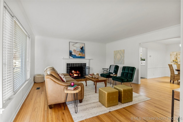 living room with visible vents, ornamental molding, wood finished floors, baseboards, and a tile fireplace