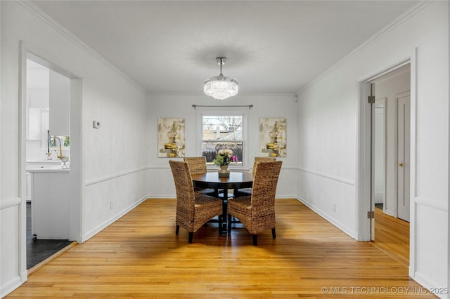 dining area with light wood-style flooring, crown molding, and an inviting chandelier