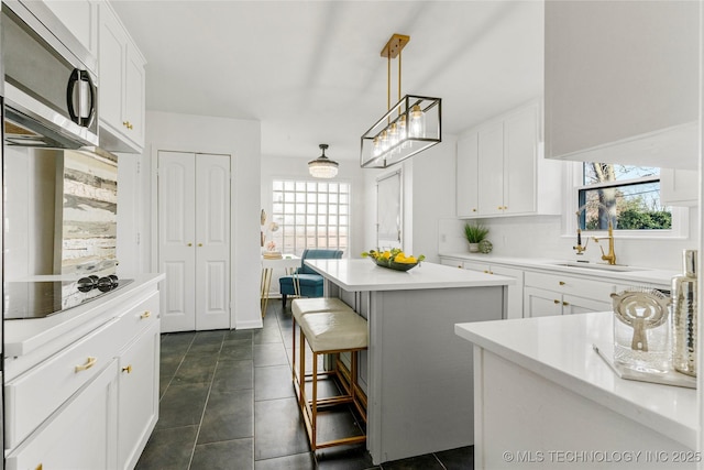 kitchen with stainless steel microwave, a center island, light countertops, black electric cooktop, and a sink