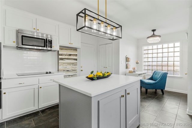 kitchen featuring stainless steel microwave, white cabinets, light countertops, decorative backsplash, and black electric stovetop