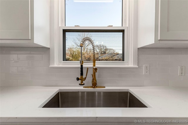 room details featuring a sink, light stone countertops, tasteful backsplash, and white cabinets