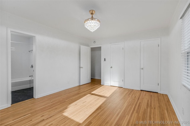 unfurnished bedroom with a notable chandelier, baseboards, and light wood finished floors