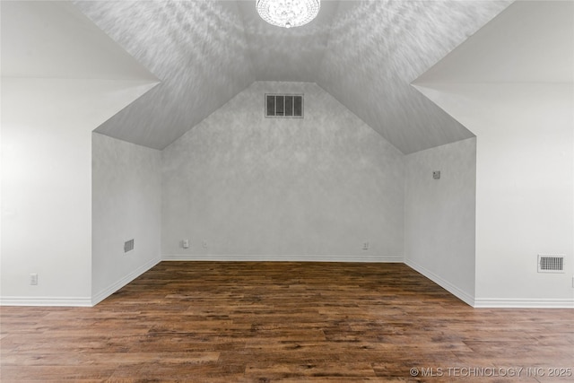 additional living space with visible vents, dark wood-type flooring, and vaulted ceiling