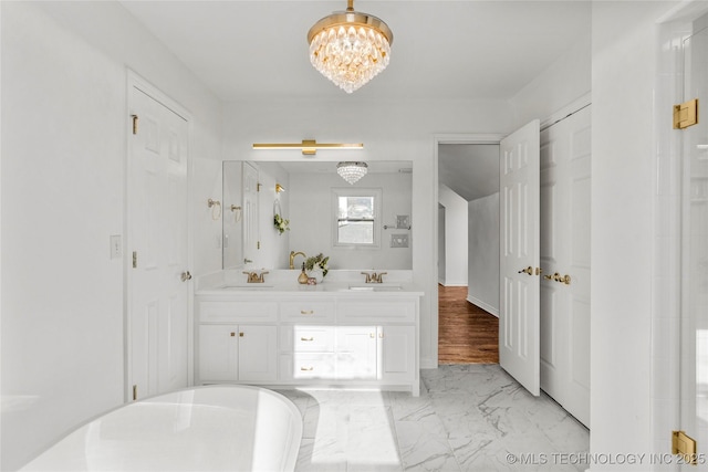 full bath with double vanity, a notable chandelier, marble finish floor, and a sink