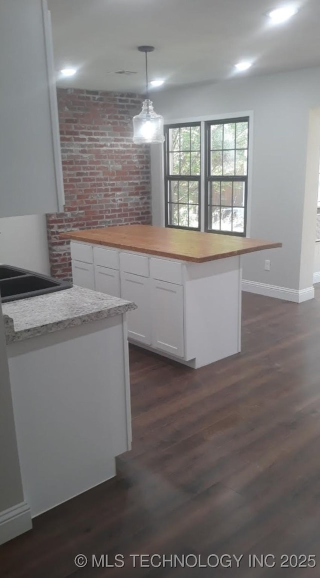 kitchen with wooden counters, dark wood finished floors, hanging light fixtures, and white cabinetry