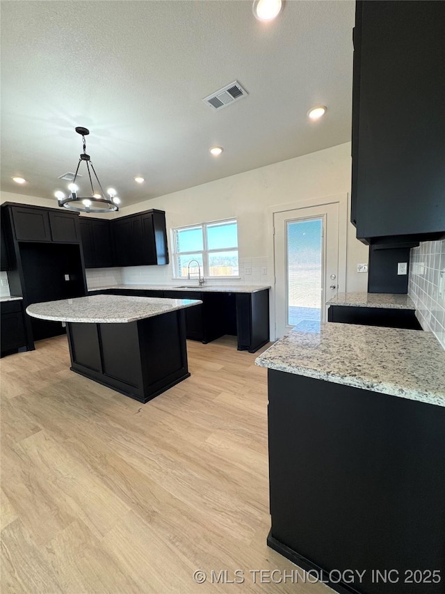 kitchen with visible vents, dark cabinetry, decorative backsplash, and a sink