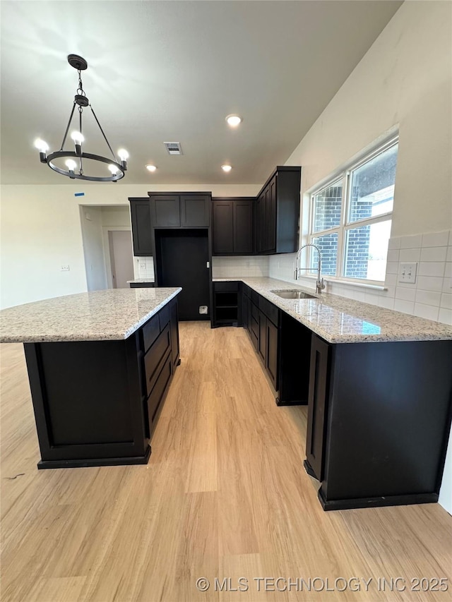 kitchen with dark cabinetry, light stone countertops, visible vents, a sink, and light wood-type flooring