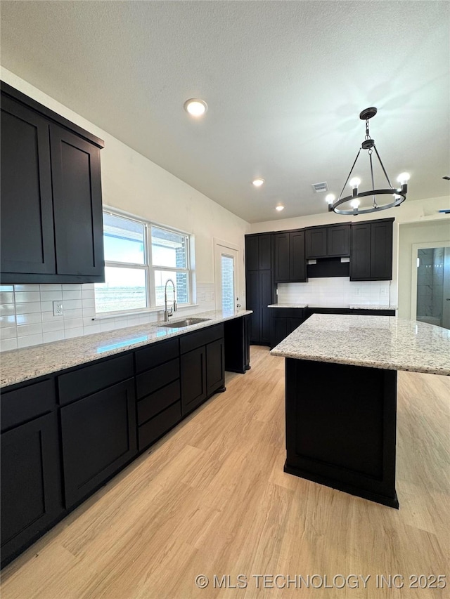 kitchen with light wood-type flooring, a sink, an inviting chandelier, decorative backsplash, and light stone countertops