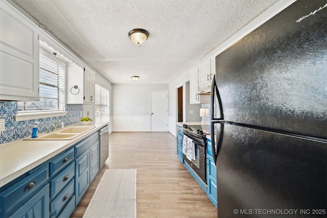 kitchen featuring blue cabinetry, freestanding refrigerator, a sink, white cabinets, and range with electric stovetop