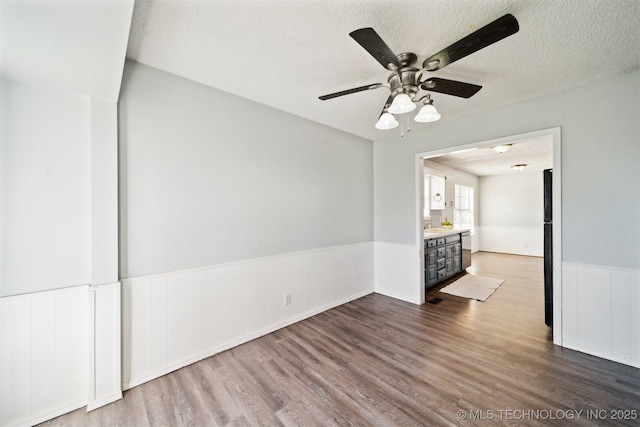 empty room with wainscoting, a textured ceiling, ceiling fan, and wood finished floors