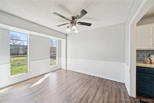 interior space with ceiling fan, a wainscoted wall, a textured ceiling, and wood finished floors