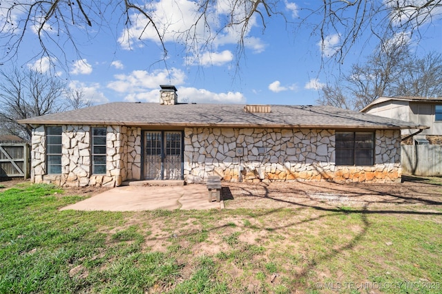 rear view of house featuring fence, a yard, a chimney, stone siding, and a patio area