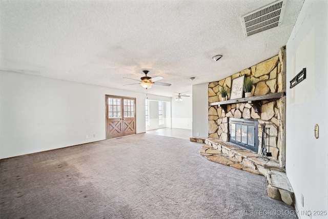 unfurnished living room with visible vents, a ceiling fan, a stone fireplace, and carpet