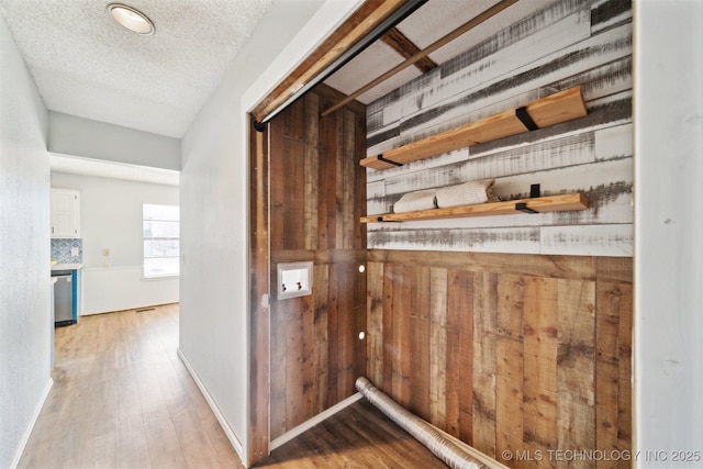 hallway featuring baseboards, a textured ceiling, wood finished floors, and wooden walls