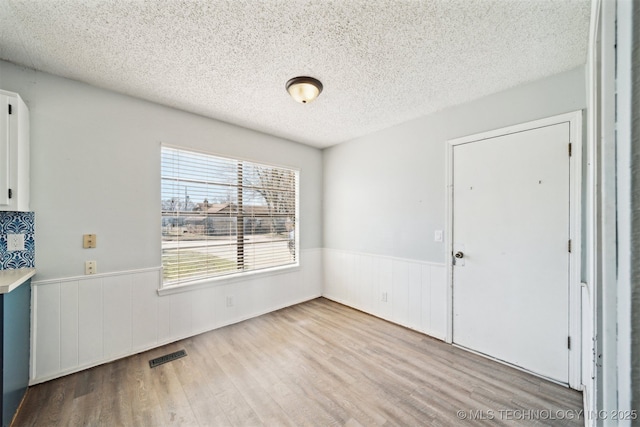 unfurnished dining area featuring visible vents, a textured ceiling, wood finished floors, and wainscoting