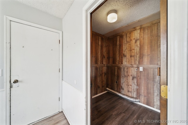 corridor with wooden walls, wood finished floors, and a textured ceiling