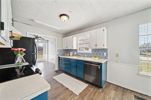 kitchen with blue cabinetry, a wainscoted wall, stainless steel dishwasher, dark wood-style floors, and a sink