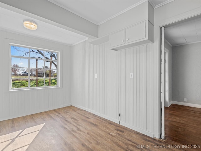 spare room featuring ornamental molding, baseboards, and wood finished floors