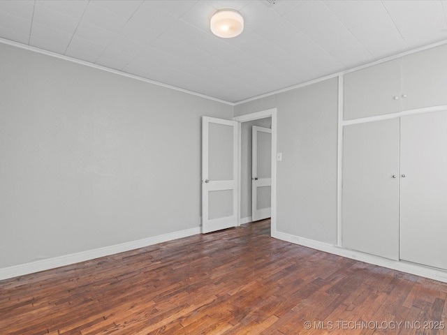 unfurnished bedroom with crown molding, wood finished floors, baseboards, and a closet