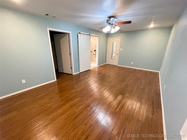 interior space featuring visible vents, baseboards, a barn door, wood finished floors, and a ceiling fan