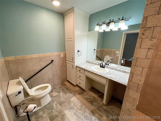 bathroom with wainscoting, vanity, toilet, and tile walls