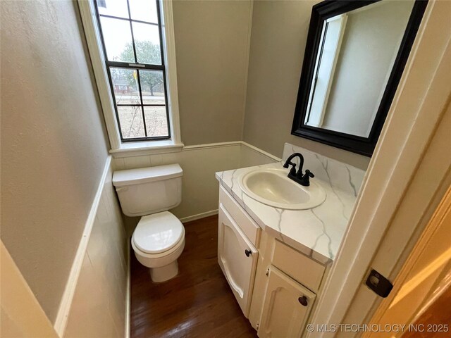 half bathroom with toilet, vanity, and wood finished floors