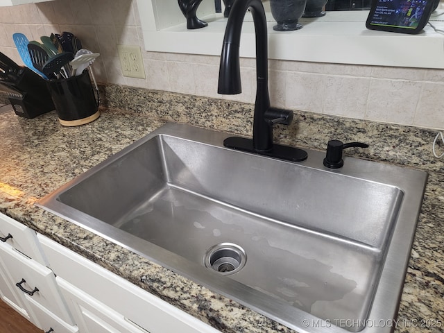 room details featuring decorative backsplash, white cabinets, and a sink