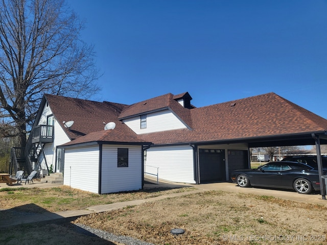 view of side of property featuring an outbuilding, stairway, a garage, and roof with shingles