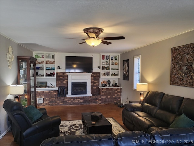 living room featuring ceiling fan, a brick fireplace, wood finished floors, and ornamental molding