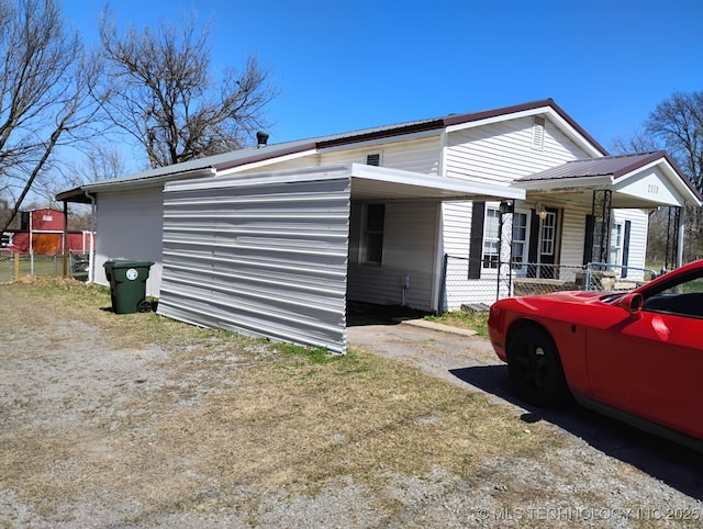 view of side of property featuring a carport, fence, and metal roof