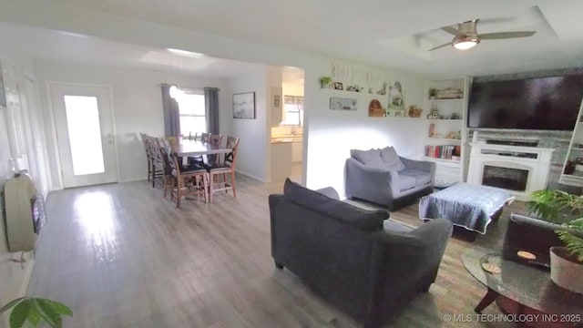 living area featuring a fireplace, a tray ceiling, wood finished floors, and ceiling fan